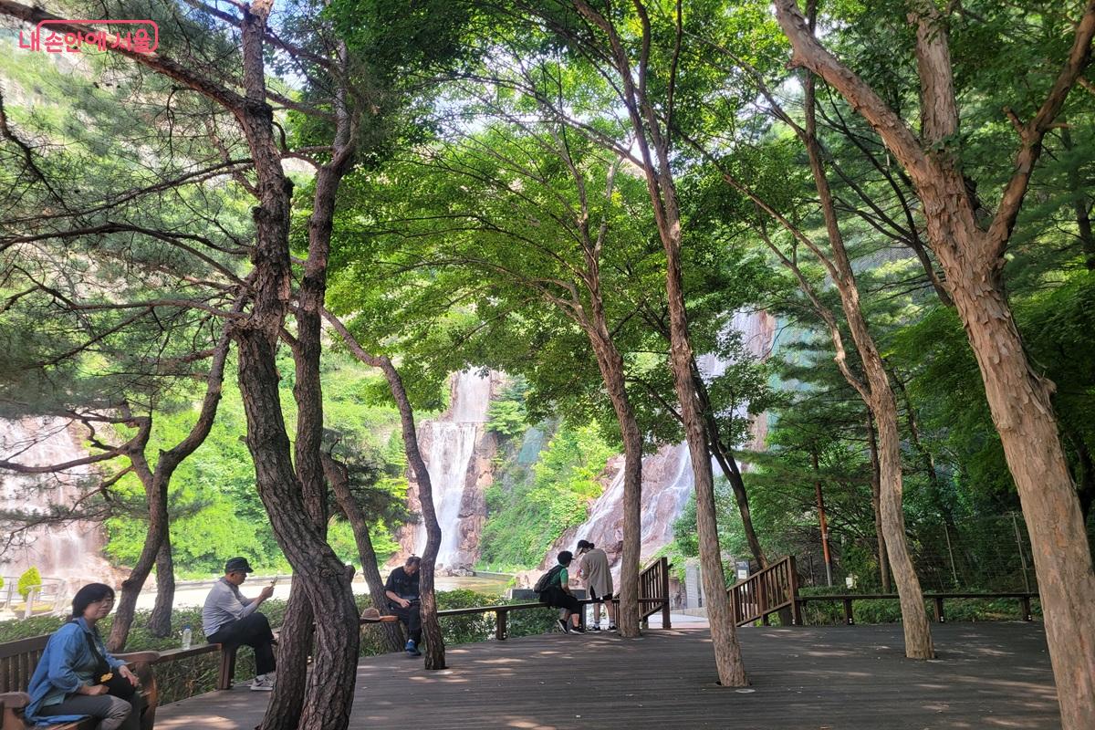 숲속 데크 쉼터에서 폭포를 바라보며 여유로운 시간을 보내는 시민들 ©조연