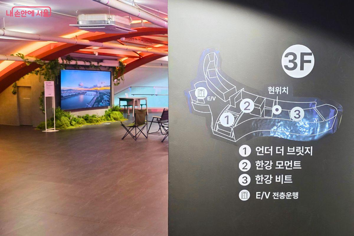 한강플플 3층 안내도와 언더 더 브릿지 체험존이 함께 보이는 모습이다. 안내도에는 언더 더 브릿지, 한강 모먼트, 한강 비트 위치가 표시되어 있으며, 뒤쪽에는 영상 화면과 의자가 놓인 휴식형 체험 공간이 보인다.