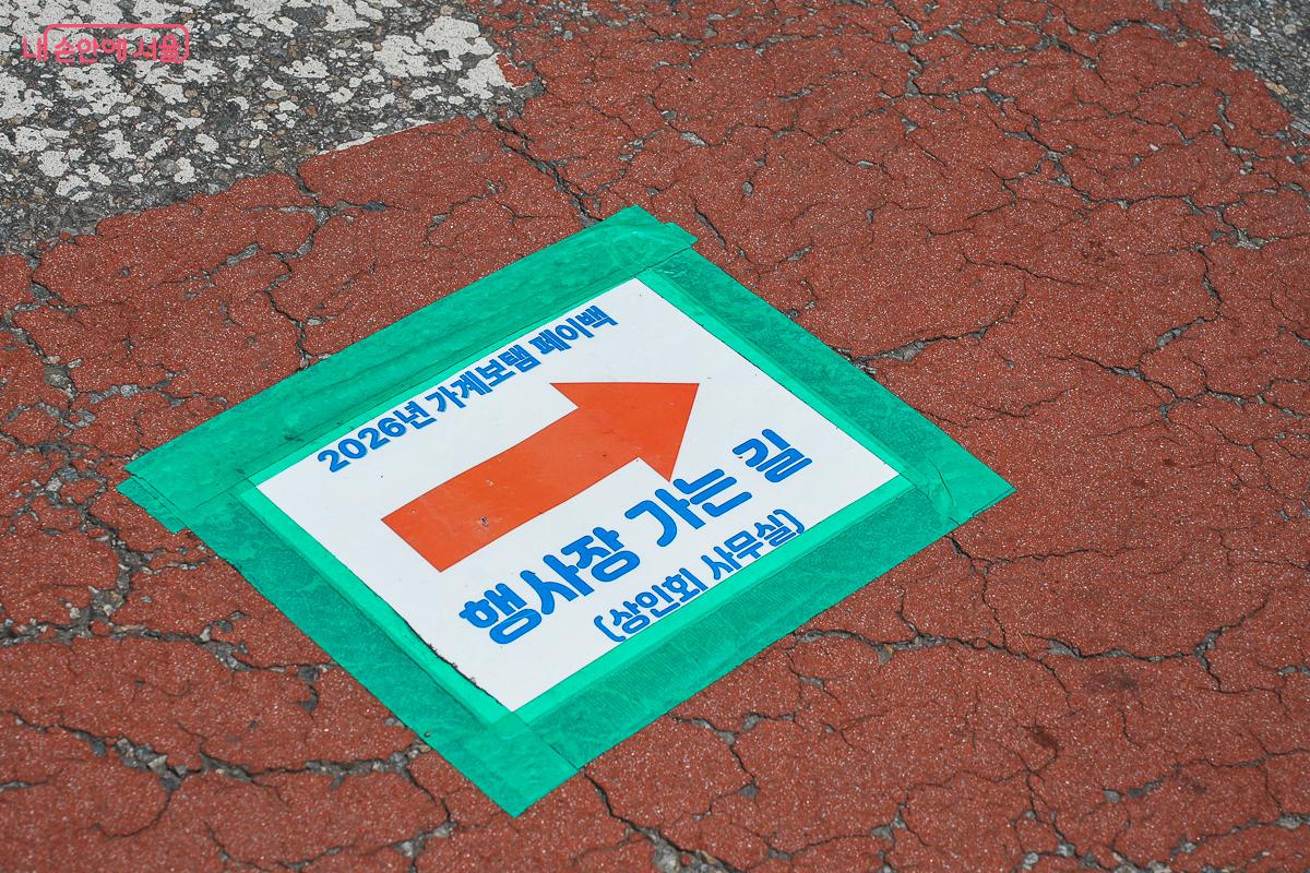 붉은 바닥에 붙은 페이백 행사장 가는 길 안내 스티커, 주황색 화살표와 상인회 사무실 안내 문구