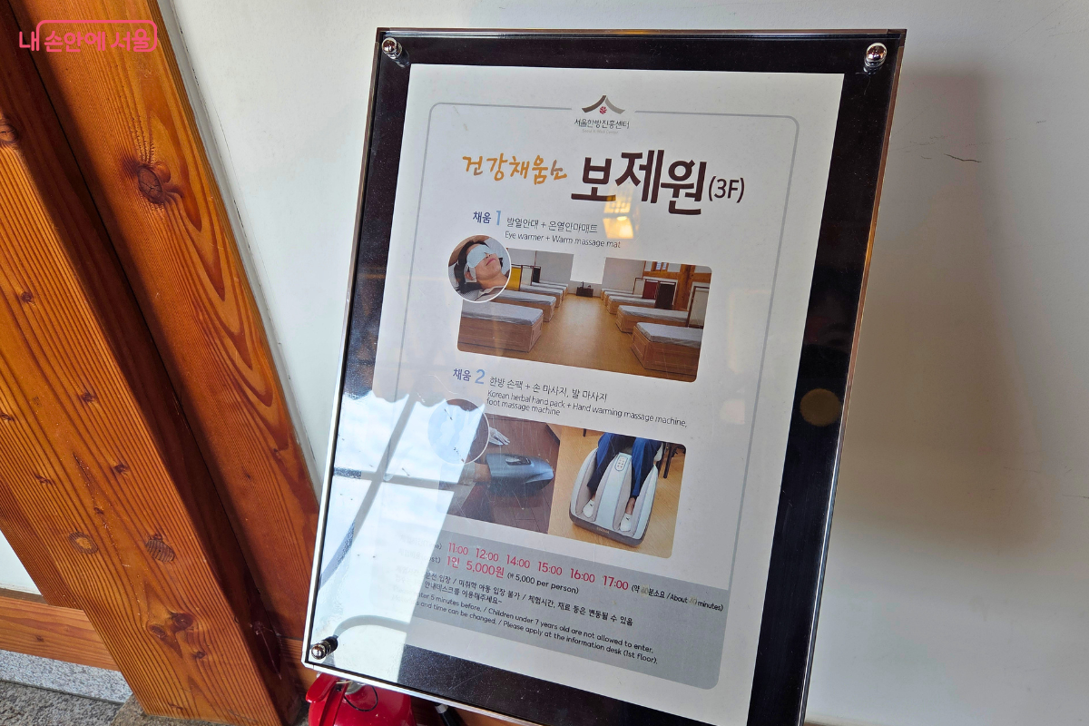 서울한방진흥센터 3층 보제원 입구 안내판이다. 안내판에는 발열안대와 온열안마매트, 한방 손팩과 손·발 마사지 기계를 이용하는 보제원 체험 내용과 운영 시간이 적혀 있다.