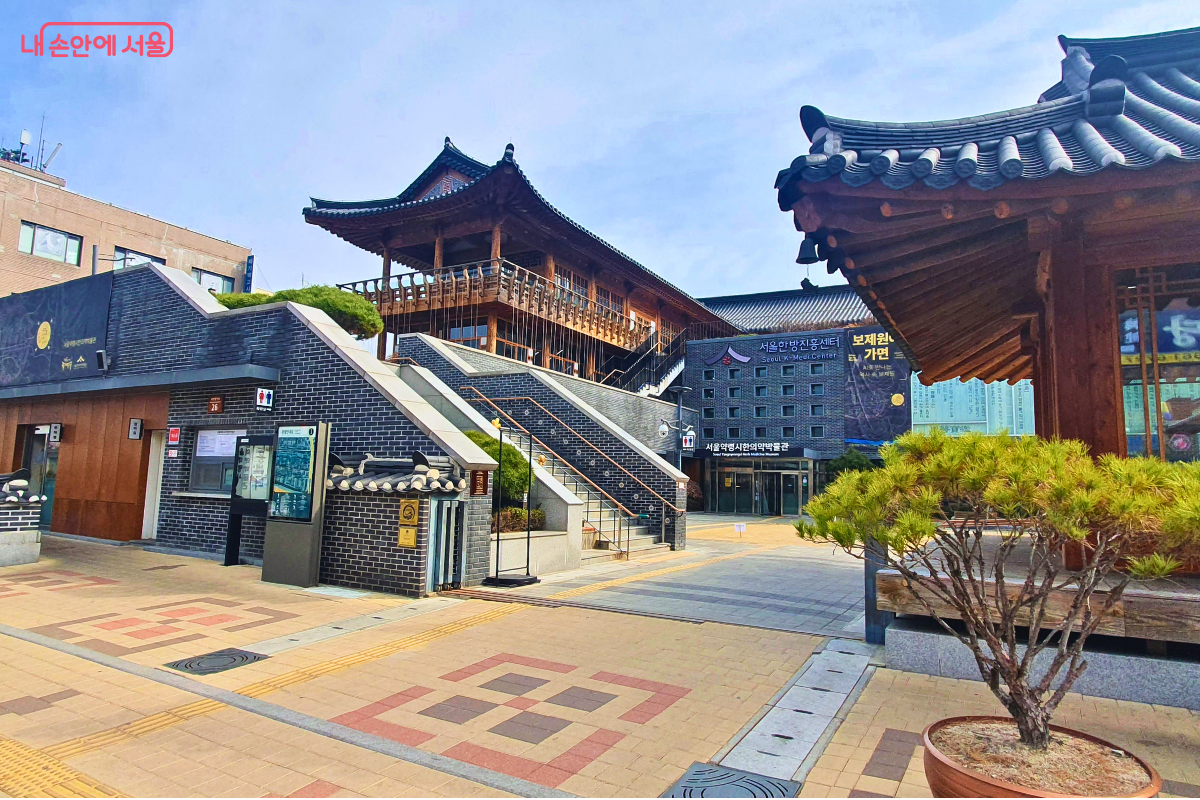 서울한방진흥센터 야외 전경이다. 전통 기와지붕과 한옥 누각, 회색 벽돌 건물이 어우러져 있고, 중앙 계단과 마당을 따라 한의약박물관과 보제원 가객관 건물이 함께 보인다.