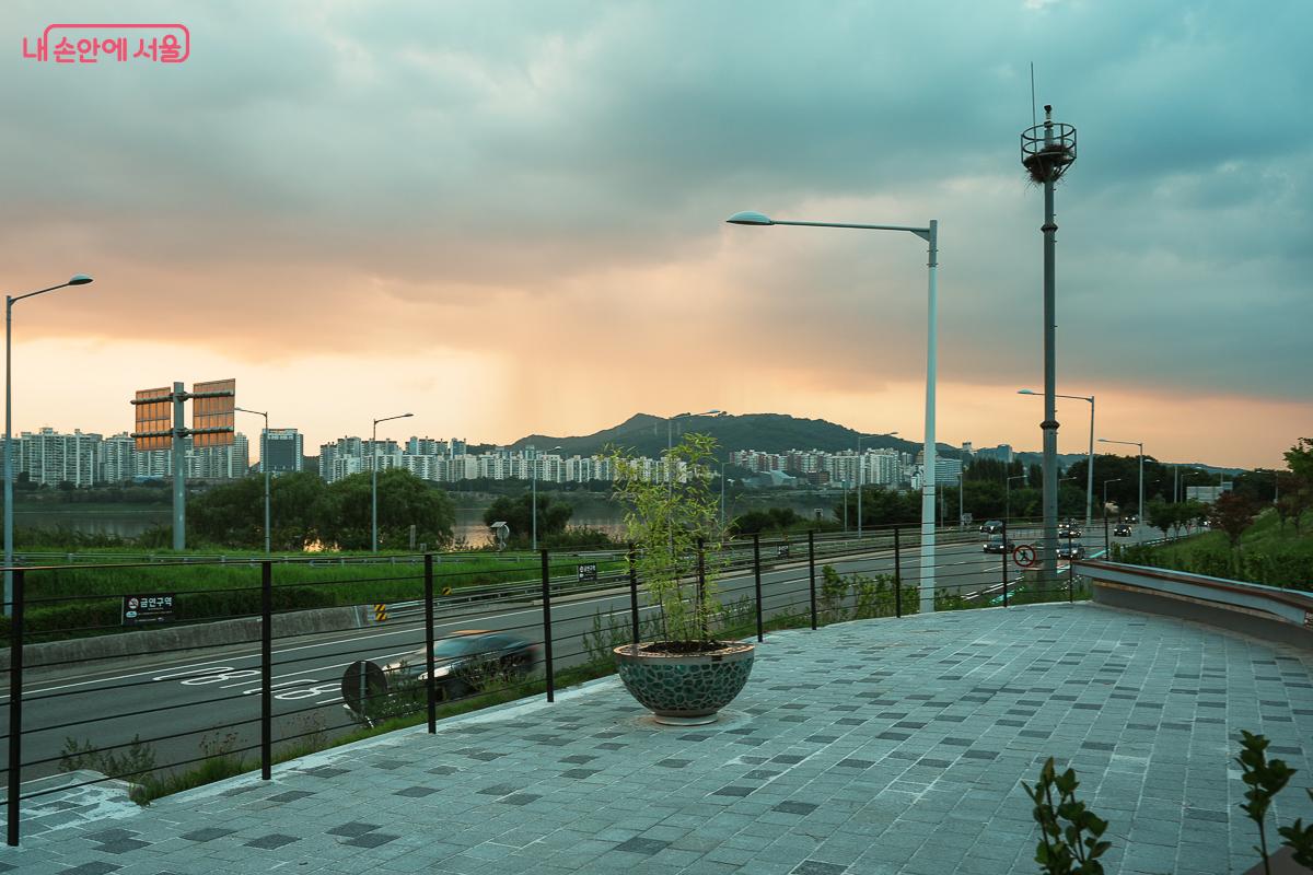 전망대 난간 옆 화분과 가로등 너머로 보이는 한강, 도로, 산 능선