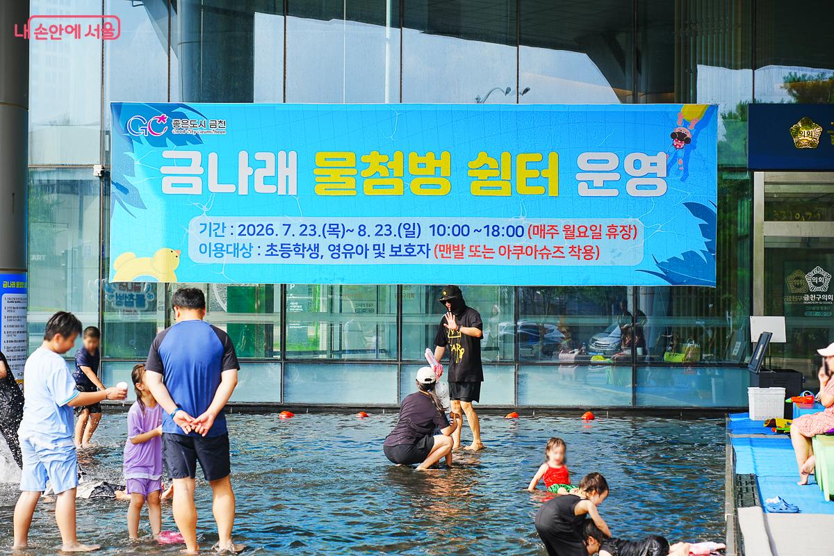 '금나래 물첨벙 쉼터 운영' 안내 배너 아래 얕은 물에서 노는 아이들과 보호자들