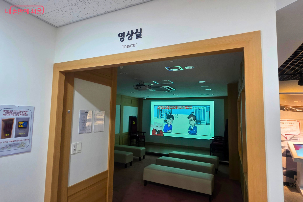 입구 너머로 헌법과 헌법재판을 설명하는 애니메이션 영상이 상영되고 있다. 실내에는 관람객이 편하게 앉아 영상을 볼 수 있도록 여러 개의 긴 의자가 나란히 놓여 있다.