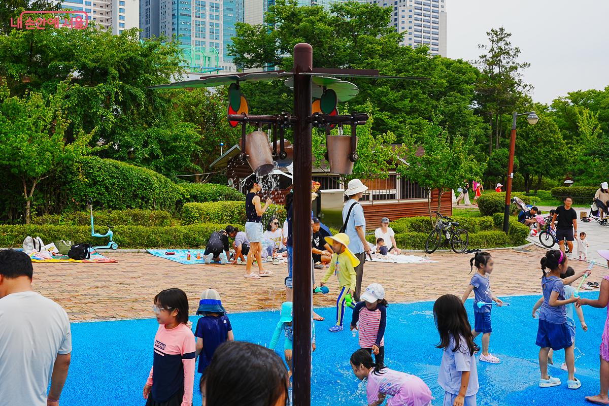 매달린 양동이 두 개가 있는 별도 물놀이 구역, 목조 건물이 배경으로 보인다.