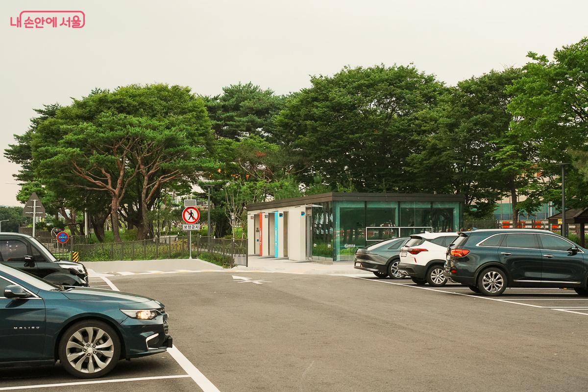 주차장 너머로 보이는 흰색 화장실&middot;휴게동 건물 전경