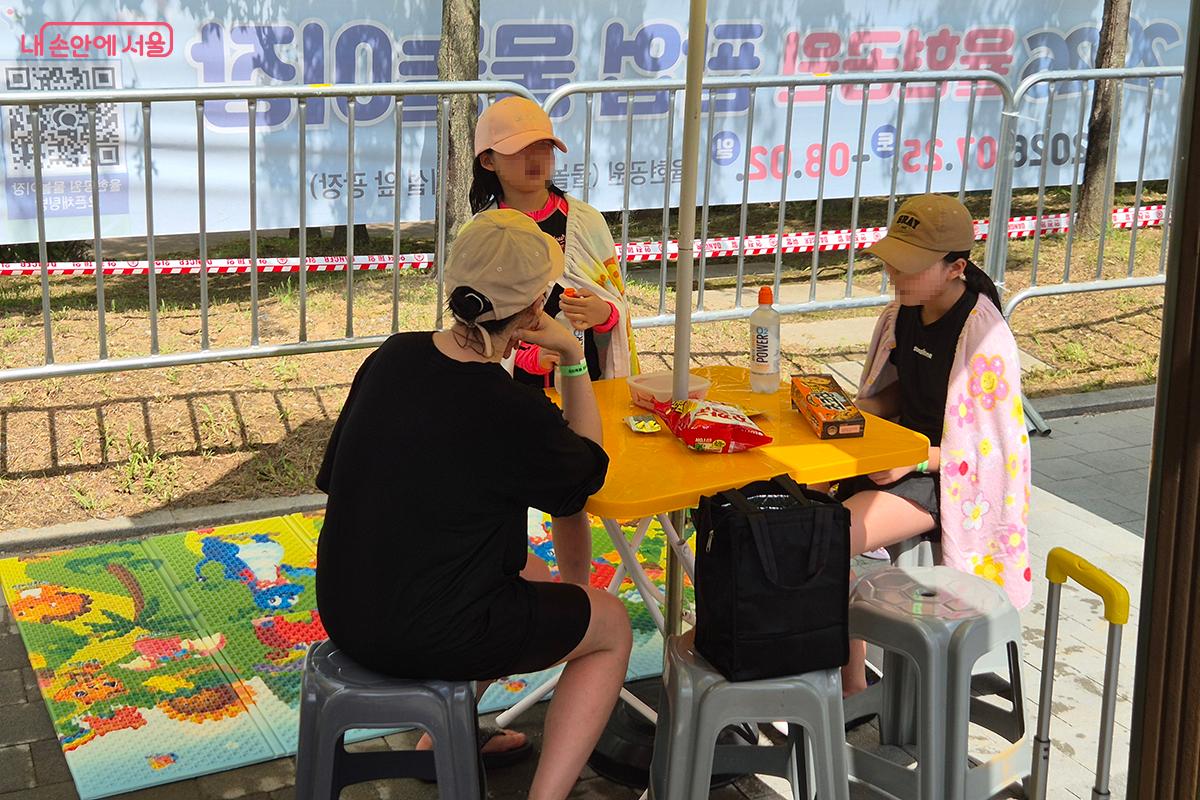 시원한 그늘 밑에서 준비해온 간단한 식음료를 즐기는 가족들