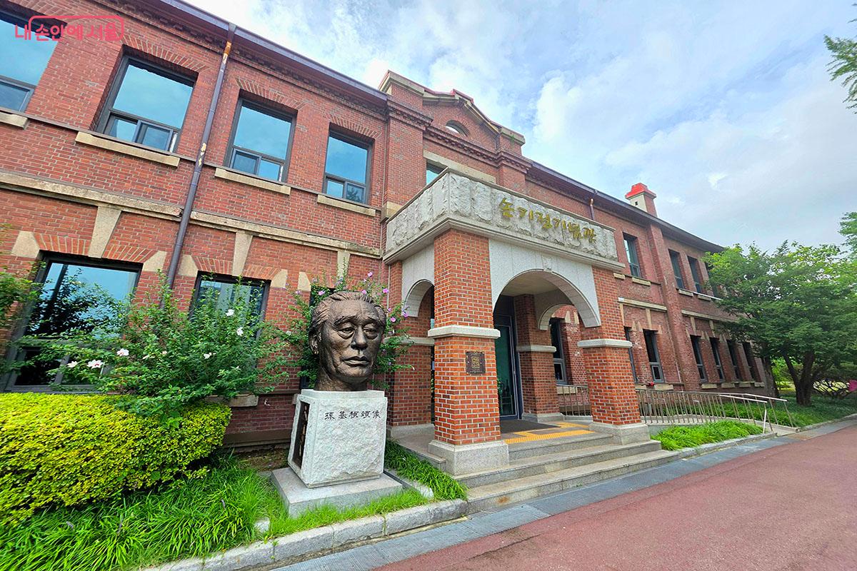 푸른 잎사귀 사이로 보이는 손기정기념관의 정겨운 붉은 벽돌 외관. 입구 왼쪽에는 손기정 선수의 숭고한 정신을 기리는 두상이 세워져 있다.