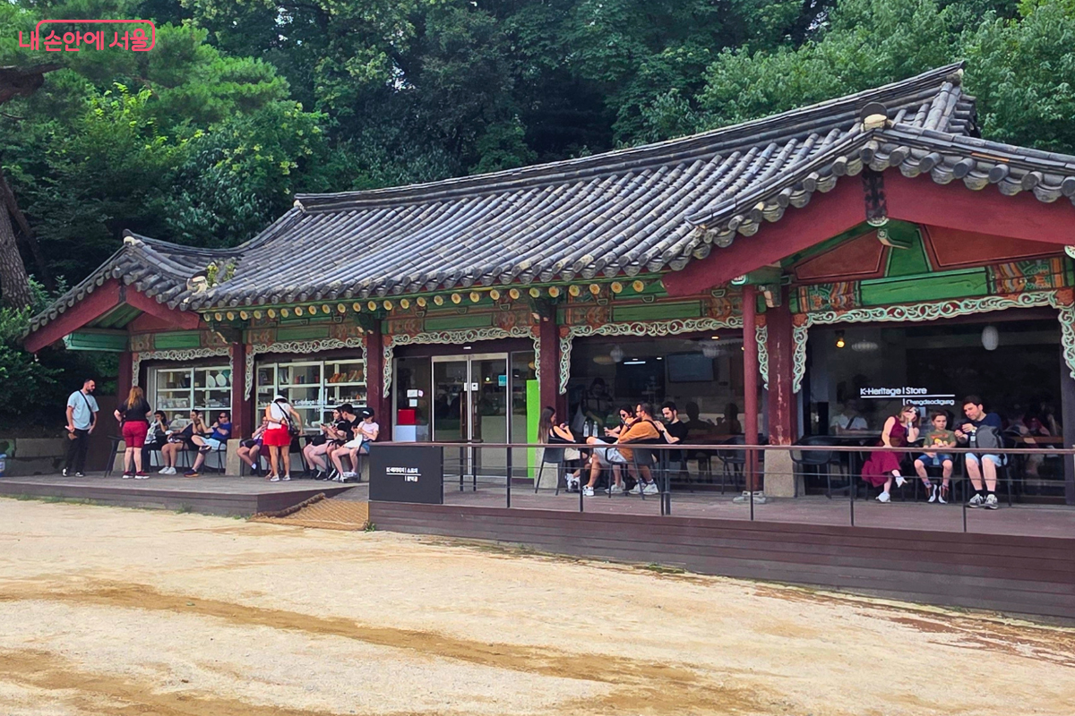창덕궁 내 휴식 공간 앞에서 여러 관람객이 음료를 마시거나 휴식을 취하고 있다.