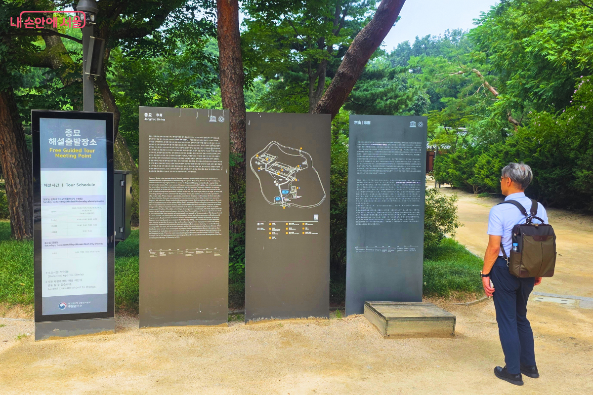 울창한 나무가 둘러싼 종묘 입구 쪽에 배낭을 멘 관람객 한 명이 안내판을 바라보며 관람 정보를 확인하고 있다.