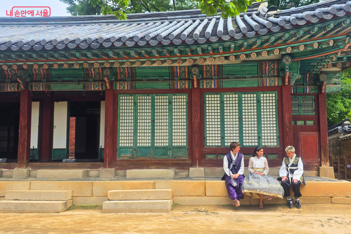 창덕궁 전각 기단에 한복을 입은 관람객 세 명이 나란히 앉아 이야기를 나누고 있다.