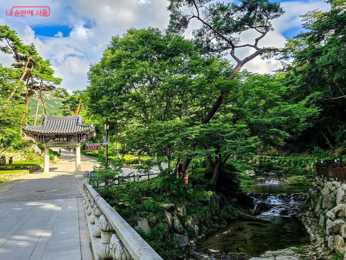 북한산 자락을 배경으로 진관사 일주문과 계곡이 어우러진 풍경. 맑은 계곡물이 사찰 경내 옆을 조용히 흘러내려온다.