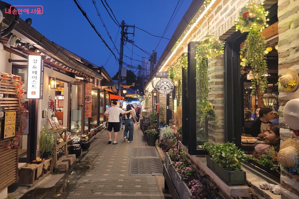 푸른 저녁 하늘 아래 한옥 기와지붕과 상점의 따뜻한 조명이 어우러진 익선동 &copy;조연