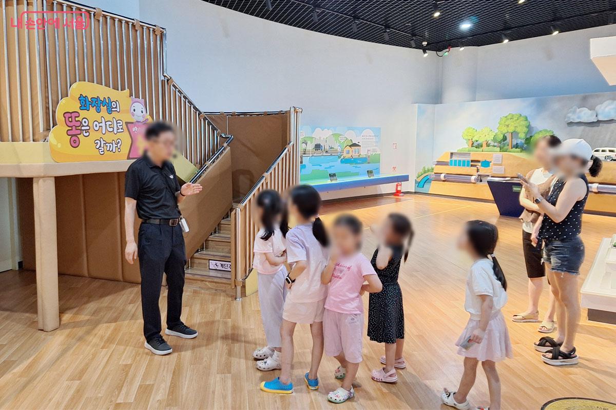 아이들이 변기 슬라이드 앞에서 '화장실의 똥은 어디로 갈까?'에 대한 설명을 듣고 있다.
