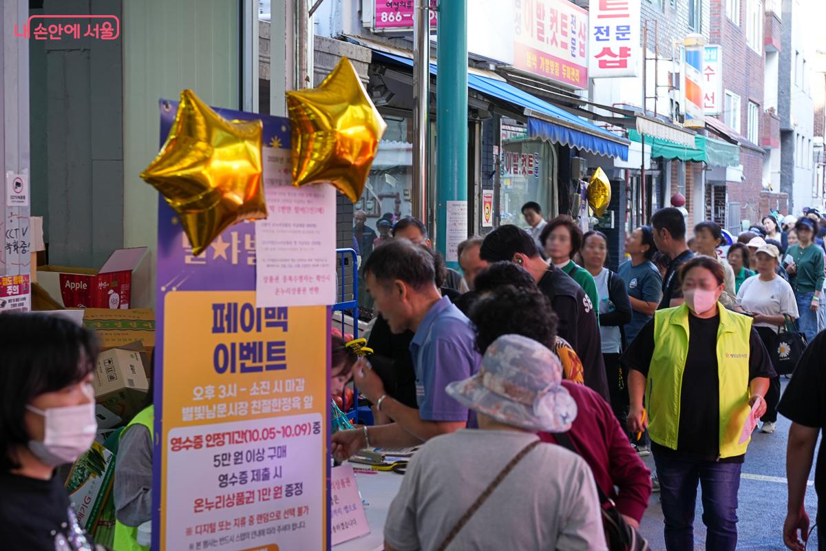 금색 별 풍선이 달린 '페이백 이벤트' 안내판과 그 앞에 길게 늘어선 대기줄
