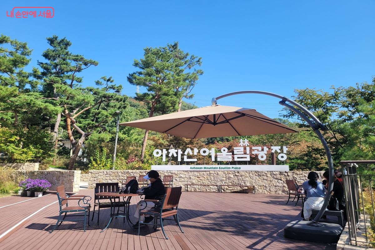 아차산어울림광장 표지 앞에 파라솔과 탁자, 의자가 놓인 휴식 공간