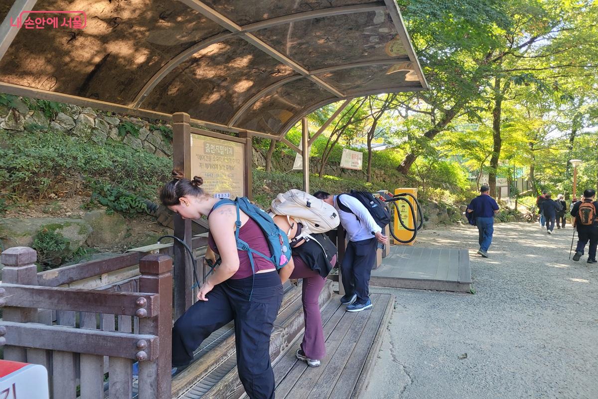 지붕이 있는 공간에서 신발의 흙을 털어내는 장치를 이용하는 사람들