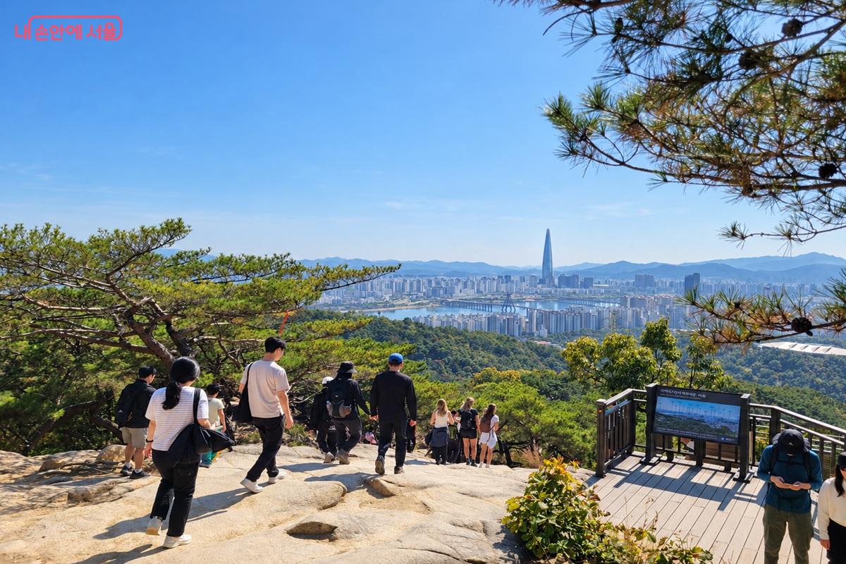 소나무와 바위가 있는 아차산 전망 구간에서 산행객들이 한강과 롯데월드타워가 보이는 서울 도심을 바라보는 모습