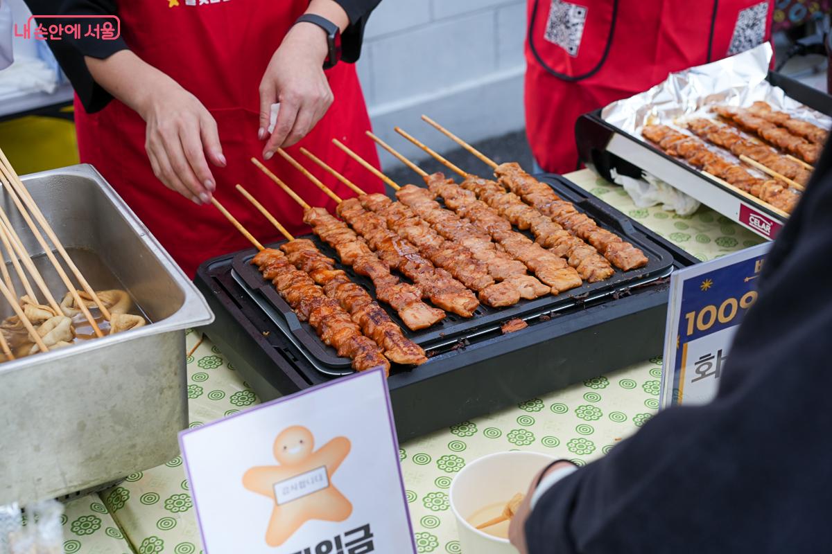 빨간 앞치마를 두른 상인이 불판 위에서 양념이 발린 꼬치를 굽는 모습