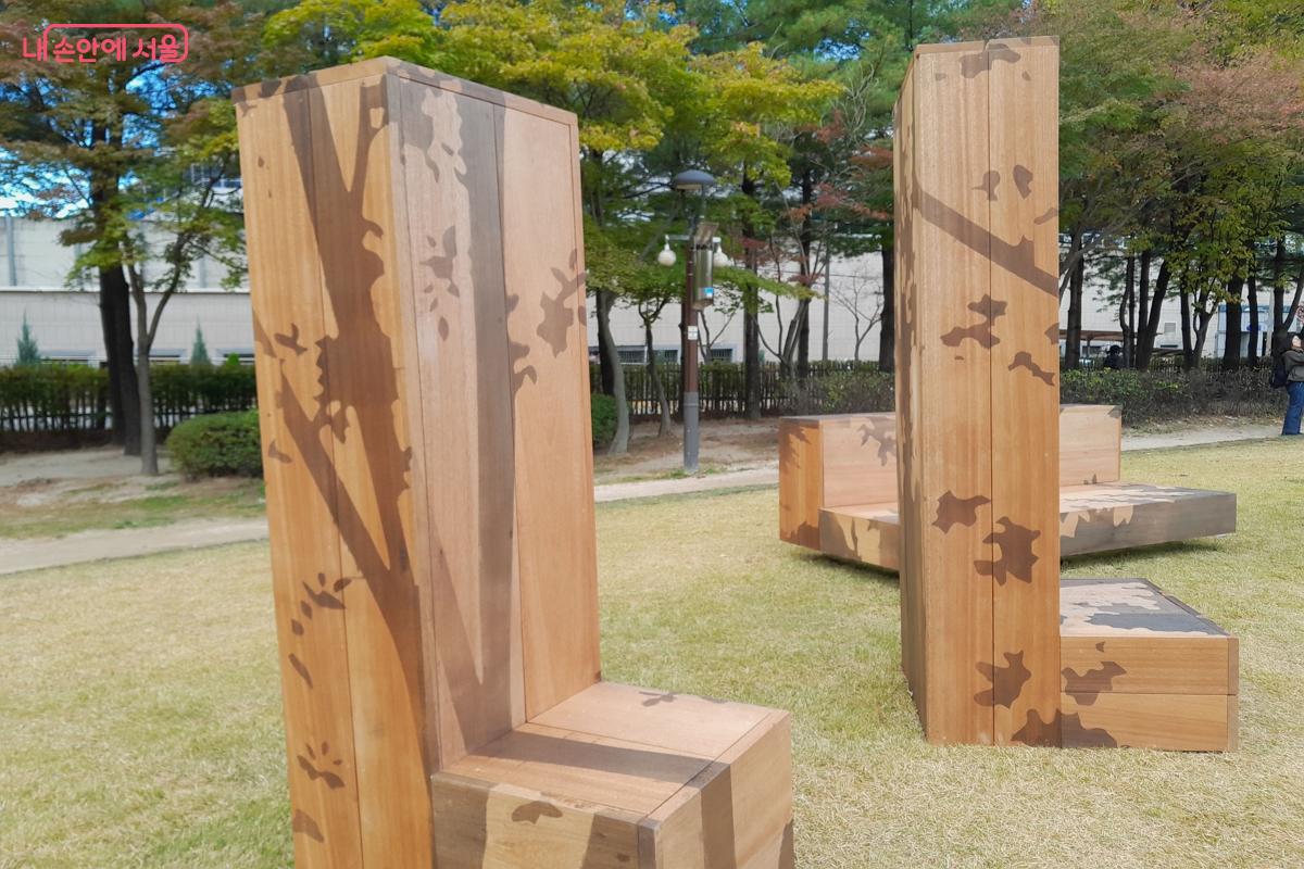 수직으로 솟아오른 목재 의자 표면에 담긴 나뭇가지와 잎사귀 그림자 문양이 돋보인다. ©강성희