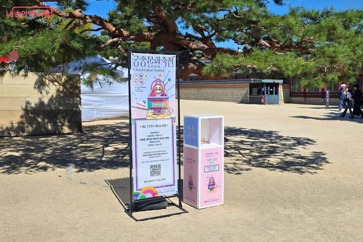 경복궁의 커다란 소나무 아래에 2026 가을 궁중문화축전 스탬프 투어 안내판이 설치돼 있다.