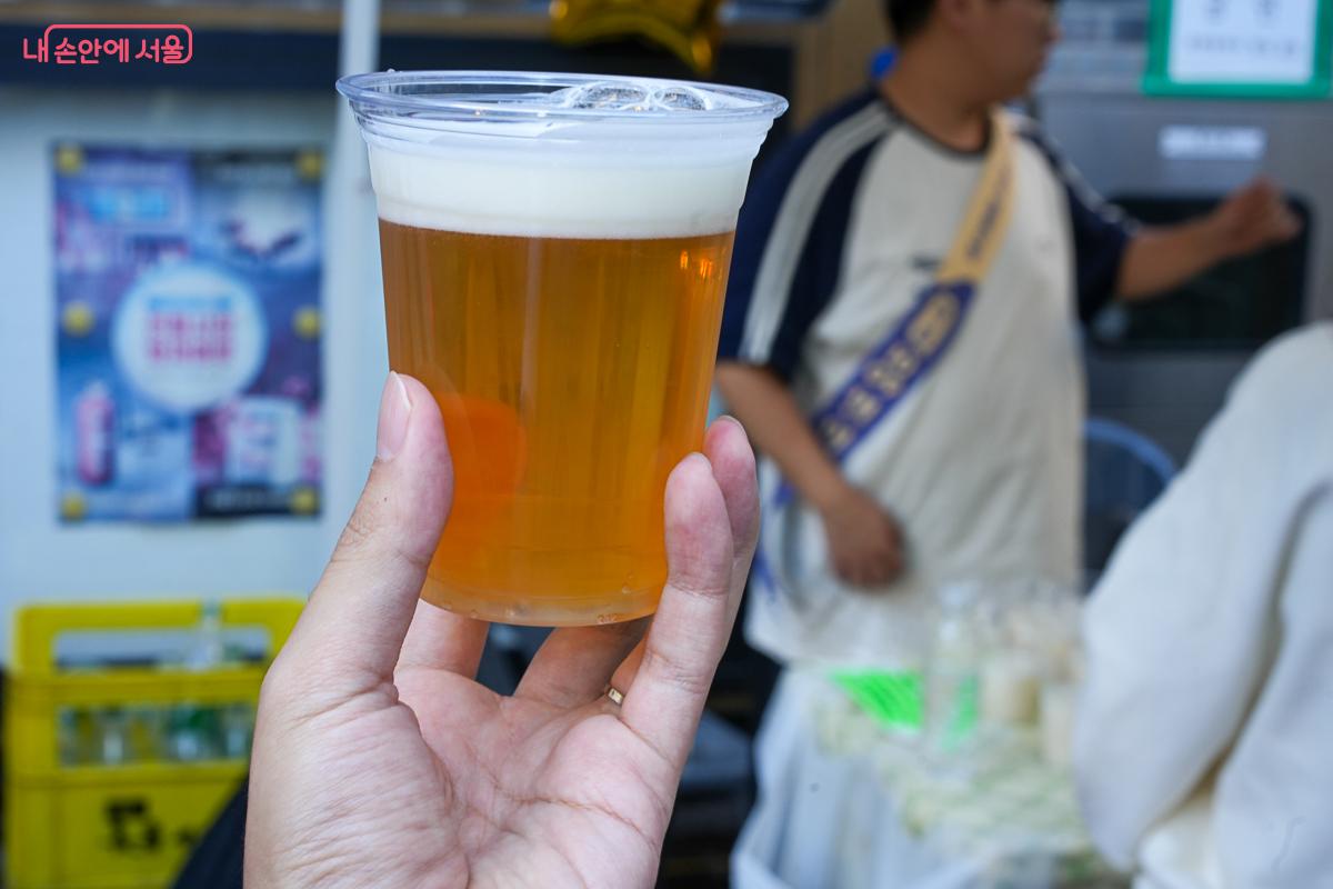 거품이 올라온 맥주가 담긴 플라스틱 컵을 손에 들고 있는 모습
