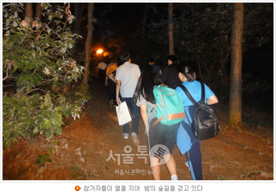 참가자들이 열을 지어 밤의 숲길을 걷고 있다