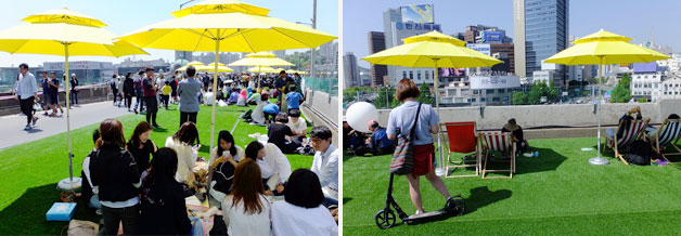 잔디밭 위 파라솔 밑 돗자리와 썬배드에서 쉬어가는 시민들