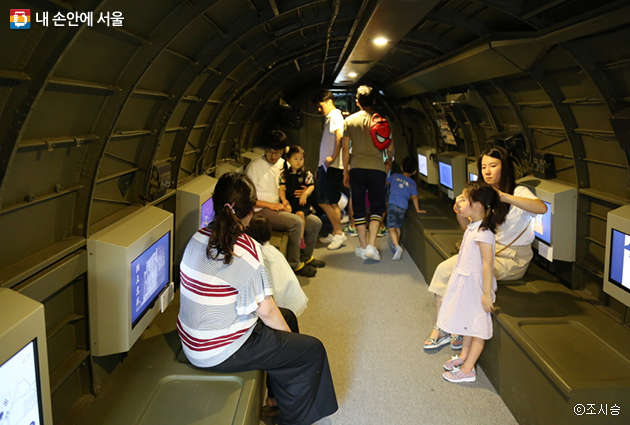 아이들과 함께 온 관람객들이 C-47 비행기서 안에서 GIF 수상작을 보고 있다