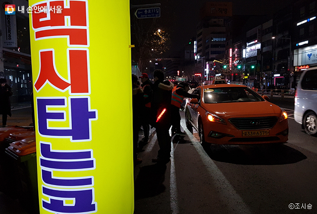 한 계도요원이 택시승차대 앞에서 승객없이 지나가는 택시를 세우고 승차거부여부를 확인하고 있다